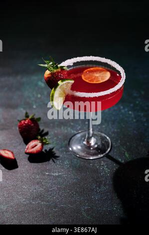 Eine lebendige Erdbeermargarita mit einem Rand aus Salz, garniert mit frischer Limette und Erdbeere auf dunkler Oberfläche. Der Cocktail fängt das Wesen ein Stockfoto