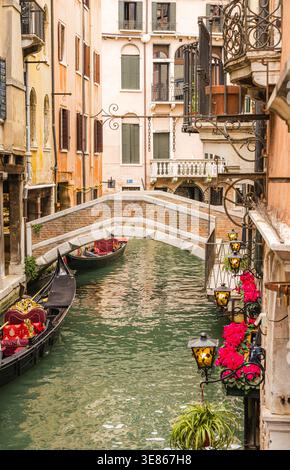 Charmanter schmaler Kanal in Venedig, Italien, mit Gondeln neben historischen Pastellgebäuden, kunstvollen Balkonen und einem kleinen bogenförmigen Steinbr Stockfoto