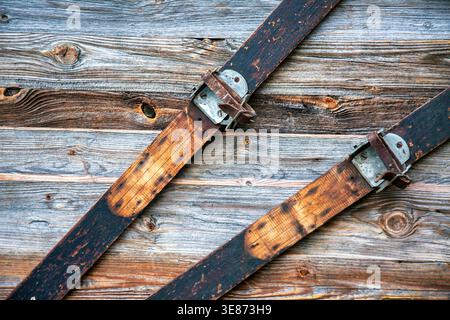 Detailgetreue Aufnahme antiker Holzskier mit authentischen Lederbindungen. Diese handgefertigte Vintage-Wintersportkunst ist an einer texturierten Holzwand montiert Stockfoto