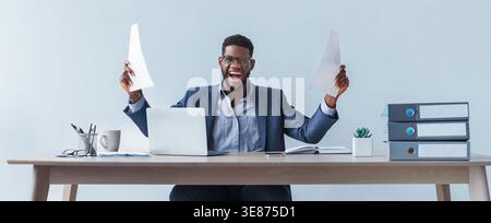 Aufgeregter Mann, der tagsüber an seinem Schreibtisch im Büro Erfolge feiert Stockfoto