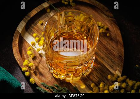 Whiskey mit Eis und Mimosa Blumen auf Holztablett International Women's Day Celebration Stockfoto