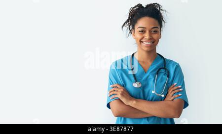 Ein lächelnder Arzt steht mit überkreuzten Armen und trägt Peeling in einem hellen Raum Stockfoto