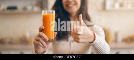 Frau genießt frischen Saft und gibt tagsüber Thumbs Up in Kitchen Setting Stockfoto