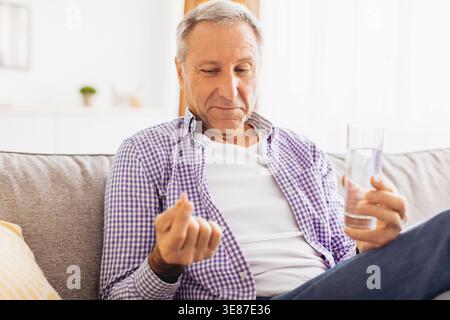 Mann, der morgens auf dem Sofa sitzt und ein Glas Wasser im Wohnzimmer hält Stockfoto