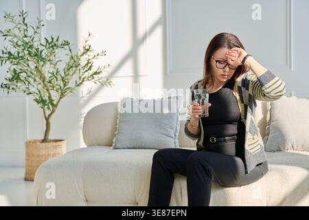 Reife traurige Frau, die Stress, mentale und körperliche Schmerzen zu Hause erlebt Stockfoto