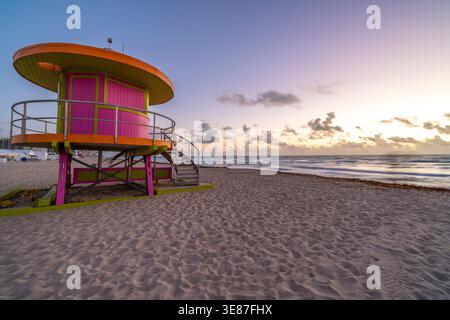 Am Strand befindet sich eine farbenfrohe Rettungsstation. Der Himmel ist eine Mischung aus rosa und orangen Tönen, die eine ruhige und friedliche Atmosphäre schaffen. Das Meer mit Stockfoto