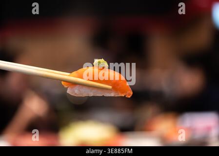 Nahaufnahme von Lachs-Sushi Nigiri gehalten von Essstäbchen mit Reis und Wasabi frische japanische Küche zarte Textur und weiche Hintergrund im Restaurant setti Stockfoto