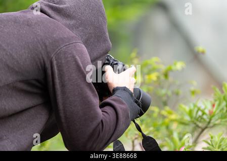 Person im Hoodie mit Kamera macht Fotos in der Natur Outdoor-Fotografie Hobby kreative Aktivität mit grünem Hintergrund Fokus auf Ausrüstung und Hände Stockfoto