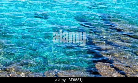 Blick von oben auf transparentes türkisfarbenes Meerwasser mit sichtbarem felsigem Meeresboden. Ruhiges, flaches mediterranes Wasser mit Sonnenlichtreflexionen und natürlicher Textur. Stockfoto