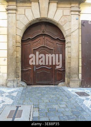 Kunstvoll geschnitzte Holztür mit einem barocken Steinbogen und klassischen Säulen, die auf einem Pflastersteinpflaster vor einem historischen Gebäude steht Stockfoto