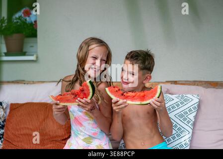 Zwei Kinder essen Wassermelone und lächeln einander an Sommertagen an Stockfoto