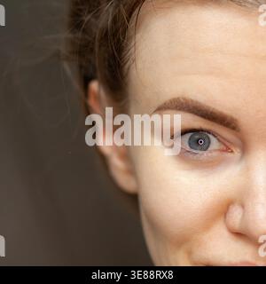 Nahaufnahme eines Porträts einer jungen Frau mit hellbraunem Haar und blauen Augen, das natürliche Schönheit und minimales Make-up vor einem verschwommenen Hintergrund zeigt Stockfoto