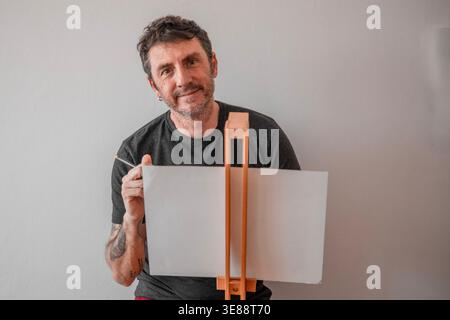 Ein Mann zeichnet mit einer Staffelei. Der Mann ist zweiundvierzig Jahre alt, kaukasischer Herkunft und wird auf hellem Hintergrund dargestellt Stockfoto