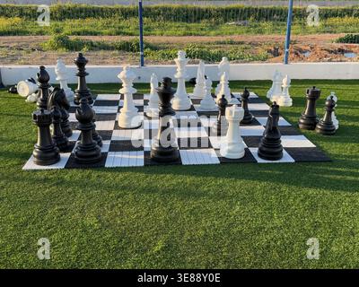 Riesige Schachfiguren, die unter Sonnenlicht auf einem Schachbrett im Freien angeordnet sind, geeignet als Hintergrund. Mobiles Foto Stockfoto