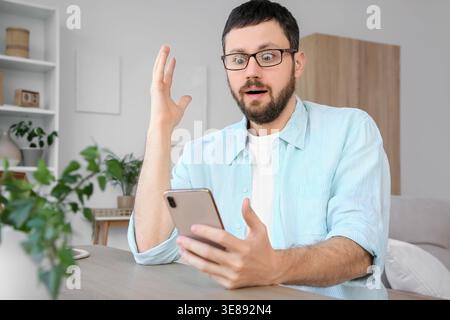 Überraschter junger Mann, der zu Hause ein Handy benutzt Stockfoto
