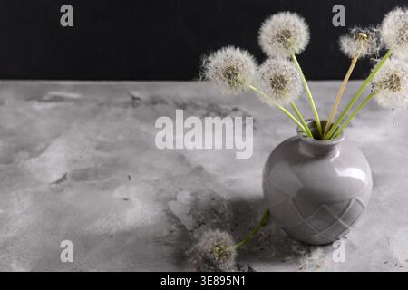 Vase mit wunderschönen Löwenzahnblumen auf dem Tisch vor dunklem Hintergrund Stockfoto
