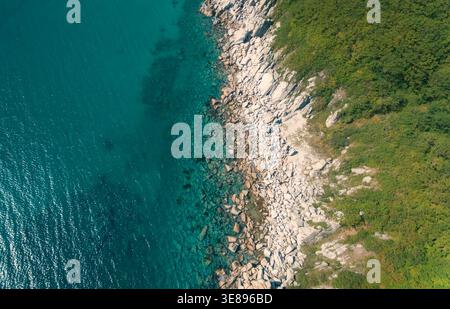 Die zerklüftete felsige Küste trifft auf klares türkisfarbenes Meereswasser und offenbart Unterwasserformationen und grüne Vegetation aus der Vogelperspektive Stockfoto