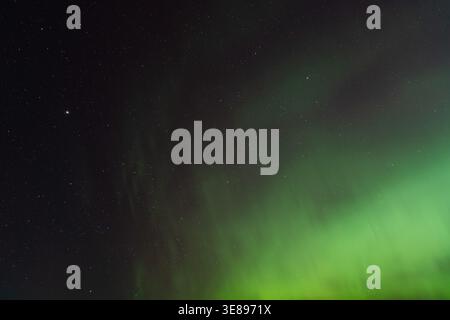 Ätherische grüne Nordlichter tanzen über dem Sternenhimmel über der ruhigen Winterlandschaft des ländlichen Estlands. Stockfoto