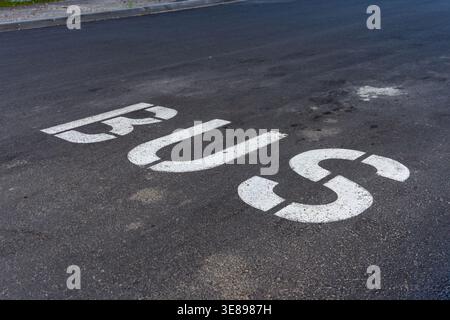 Eine Straßenmarkierung zeigt das Wort Bus auf der Asphaltoberfläche einer Stadtstraße. Die Buchstaben sind groß und klar vor der dunklen Straße. Da sind keine Autos drin Stockfoto