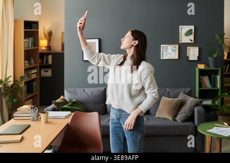 Junge Erwachsene kaukasische Frau, die ihr Smartphone hochhebt und Selfie-Videos im Home Office aufnimmt, um Inhalte in sozialen Medien zu erstellen. Nützlich für Fernarbeit, Influencer-Marketing, digitale Kommunikation Stockfoto