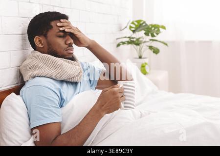 Sick african-american man trinken heißen Heilung Kaffee im Bett Stockfoto