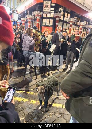 Carol-Sänger treten vor dem Coach & Horses Pub in Soho, London auf und halten eine festliche Winterszene mit traditioneller Weihnachtsstimmung fest Stockfoto