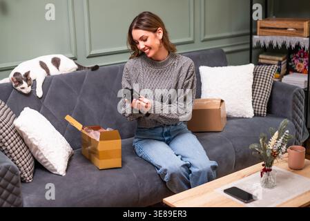 Eine fröhliche Frau, die sich Parfüms ansah, die sie online kaufte und im Paket geliefert wurde. Stockfoto