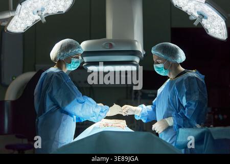 Weite Aufnahme von Chirurgen, die Operationen unter chirurgischem Licht durchführen und Instrumente im Operationssaal austauschen. Medizinisches Teamwork-Konzept für Gesundheitswerbung, Krankenhausdienstleistungen, Chirurgie Stockfoto