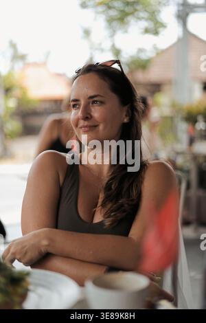 Junge lächelnde Frau mit gekreuzten Armen, die im Café im Freien auf bali sitzt Stockfoto