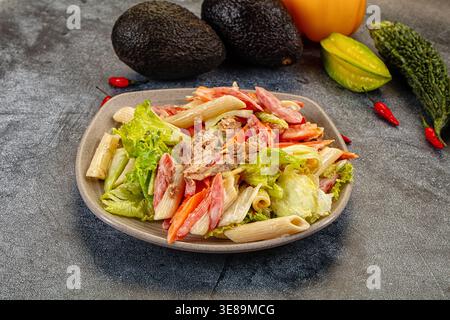 Appetitlicher Nudelsalat mit Thunfisch und Gemüse in einer cremigen Sauce. Die Top-Down-Ansicht auf dunklem Hintergrund hebt frische rote, grüne und beige Farben hervor. P Stockfoto