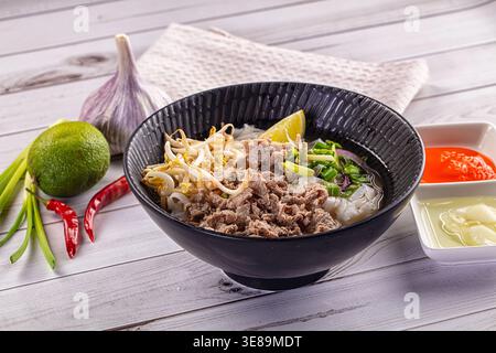 Aromatische Schüssel mit traditionellem vietnamesischem Pho Bo mit Rindfleisch, Nudeln und Sojasprossen. Serviert mit Limette, Chili und Knoblauch auf weißem Holzhintergrund. F Stockfoto