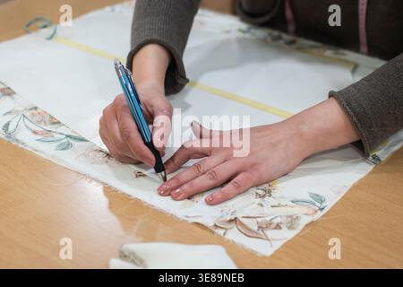 Nahaufnahme des Handschnitts und Markierens von Gewebe während des handgefertigten Bekleidungsprozesses im Atelier. Stockfoto