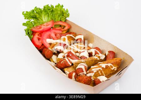 Ein lebhaftes Gericht mit knusprigen Kartoffelscheiben und scharfen Würstchen wird mit cremiger Sauce getränkt, begleitet von frischem Salat und Reifen Tomatenscheiben auf einer Brig Stockfoto