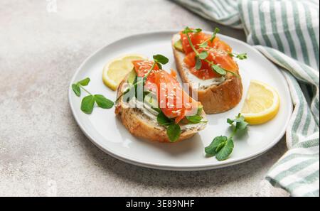Zwei gesunde Mini-Sandwiches mit Räucherlachs, Avocado, Frischkäse und Erbsensprossen auf einem Teller Stockfoto