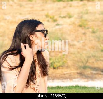 Eine junge Frau mit Sonnenbrille, die sich an einem sonnigen Sommertag in lässiger Kleidung entspannt Stockfoto