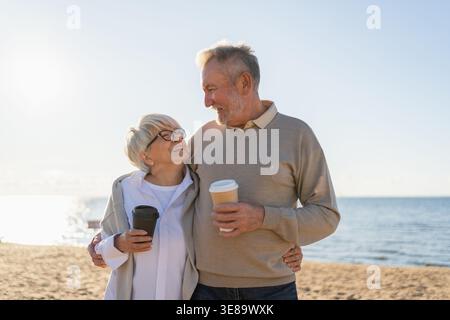 Guten Morgen. Älteres Ehepaar genießt es, mit Pappbecher Kaffee zu laufen. Die alte Ehefrau trinkt Kaffee, um nach draußen zu gehen. Großmutter Großvater macht gemeinsam spazieren. Familienmoment der Liebe Stockfoto