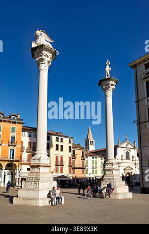 Die Gäste genießen Freizeit auf der Piazza dei Signori in Vicenza. Zwei hohe Säulen stehen im Hintergrund unter einem klaren blauen Himmel. Stockfoto