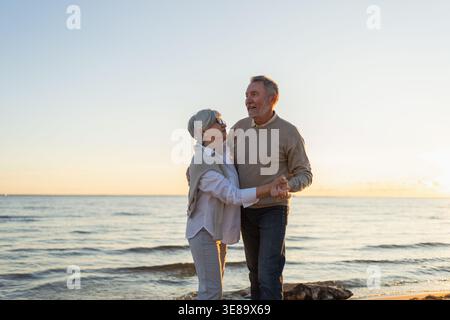 Bleiben Sie in Bewegung. Romantisches älteres Ehepaar, das gemeinsam am Strand im Freien tanzt. Glückliche lächelnde Familie pensionierter Mann Frau Ehemann Frau, die Spaß hat, die Zeit zusammen zu genießen. Familie Moment Liebe Pflege Stockfoto