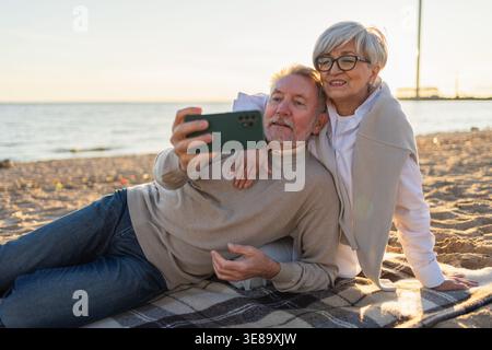 Videoanruf. Seniorenpaar, das Selfie macht, mit Videoanruf am Strand draußen. Großvater spricht online. Moderne Technologie der älteren Generation. Online-Chat für virtuelle Meetings Stockfoto