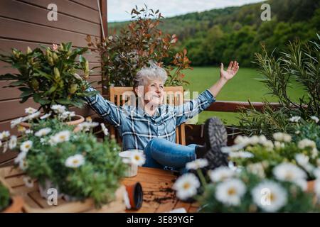 Ältere Frau mit Kaffee, die auf der Terrasse sitzt und nach der Gartenarbeit ausgeruht ist. Stockfoto