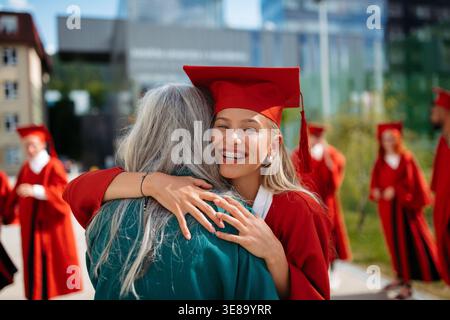 Großmutter umarmt Enkelin nach erfolgreicher Abschlussfeier im Freien. Stockfoto
