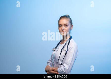 Ärztin mit weißem Mantel und Stethoskop vor blauem Hintergrund Stockfoto