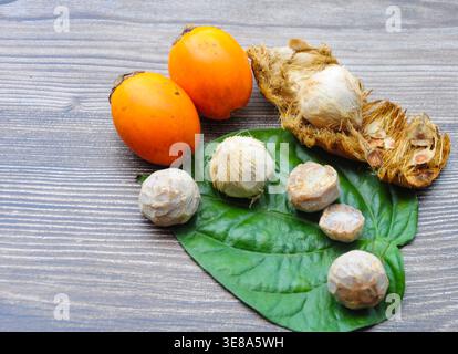 Frische orange-grüne Betelnüsse mit geöffneten Betelnussschalen auf einem gereiften Holzhintergrund in einer natürlichen Ernteanordnung. Stockfoto