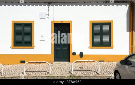 Traditionelle portugiesische Hausfassade mit weißen Wänden, gelben Zierleisten, grünen Türen und Fensterläden in der Region Alentejo Ferragudo Stockfoto