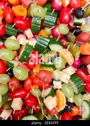 Blick von oben auf verschiedene Häppchen mit Gemüse, Obst, Käse und Würstchen auf Holzspießen, Partyessen und Vorspeisen Stockfoto