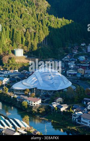 Blick aus der Vogelperspektive auf die moderne Dome Arena in Small Mountain Village am Fluss und Wald Stockfoto