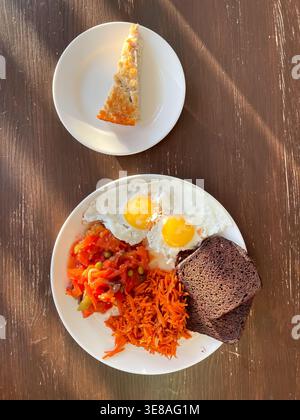 Blick von oben auf den Teller mit ausgewogener Mahlzeit aus Spiegeleiern, Roggenbrot, gedünstetem Gemüse, Karottensalat und Hüttenkäse-Auflauf, gesunder Ernährung und Nährstoffen Stockfoto