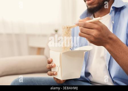 Junger afroamerikanischer Mann, der zu Hause asiatisches Essen isst Stockfoto