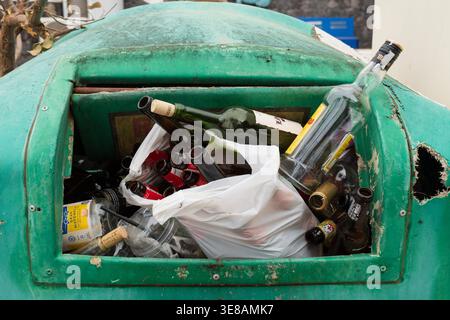 Nahaufnahme eines grünen Recyclingbehälters, der mit leeren Glasflaschen, Plastikbechern und anderen Abfallmaterialien gefüllt ist Stockfoto