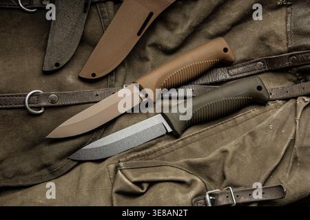Zwei taktische Überlebensmesser mit Hüllen auf einem getragenen Canvas-Rucksack mit Lederriemen. Stockfoto